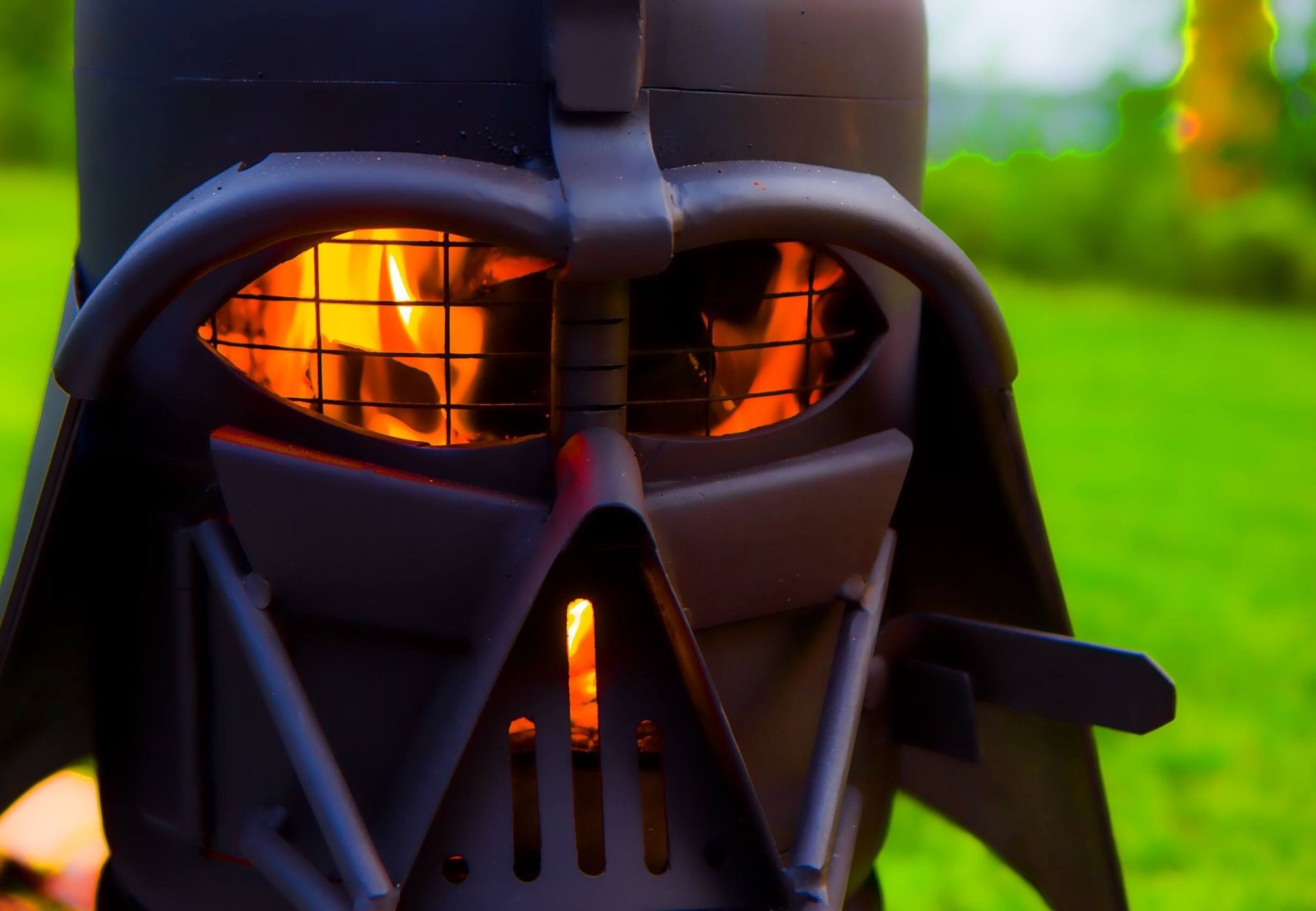 A custom made Star Wars Darth Vader fire pit with flames in the eyes, close up, with grass background